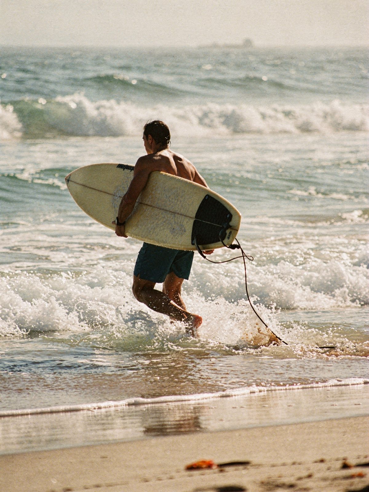 Surfer running into small waves at a sunny beach break