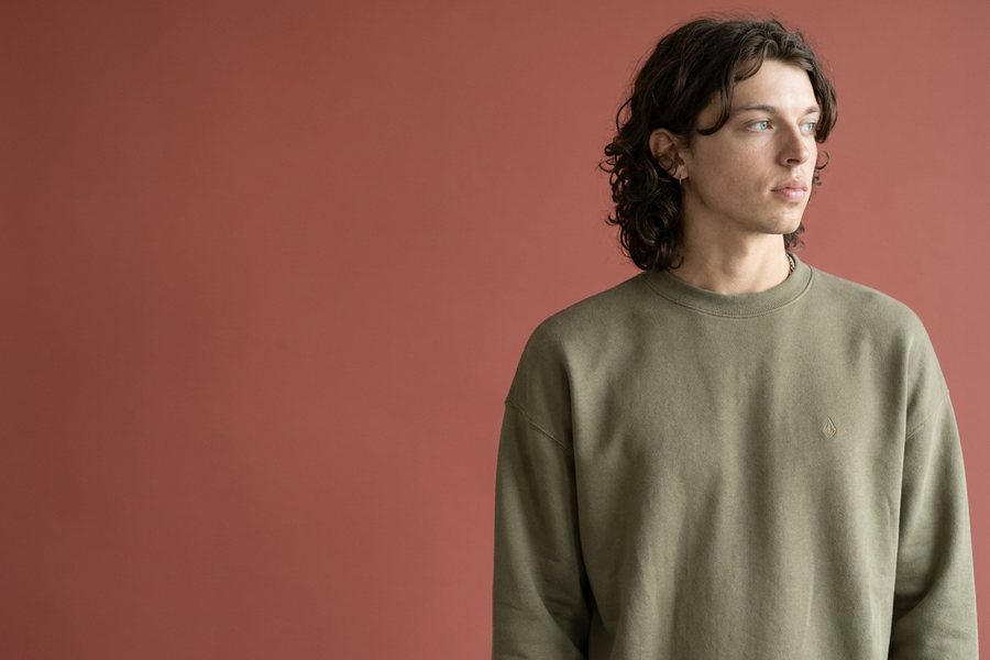 Man in an olive Volcom crew sweater against a terracotta backdrop