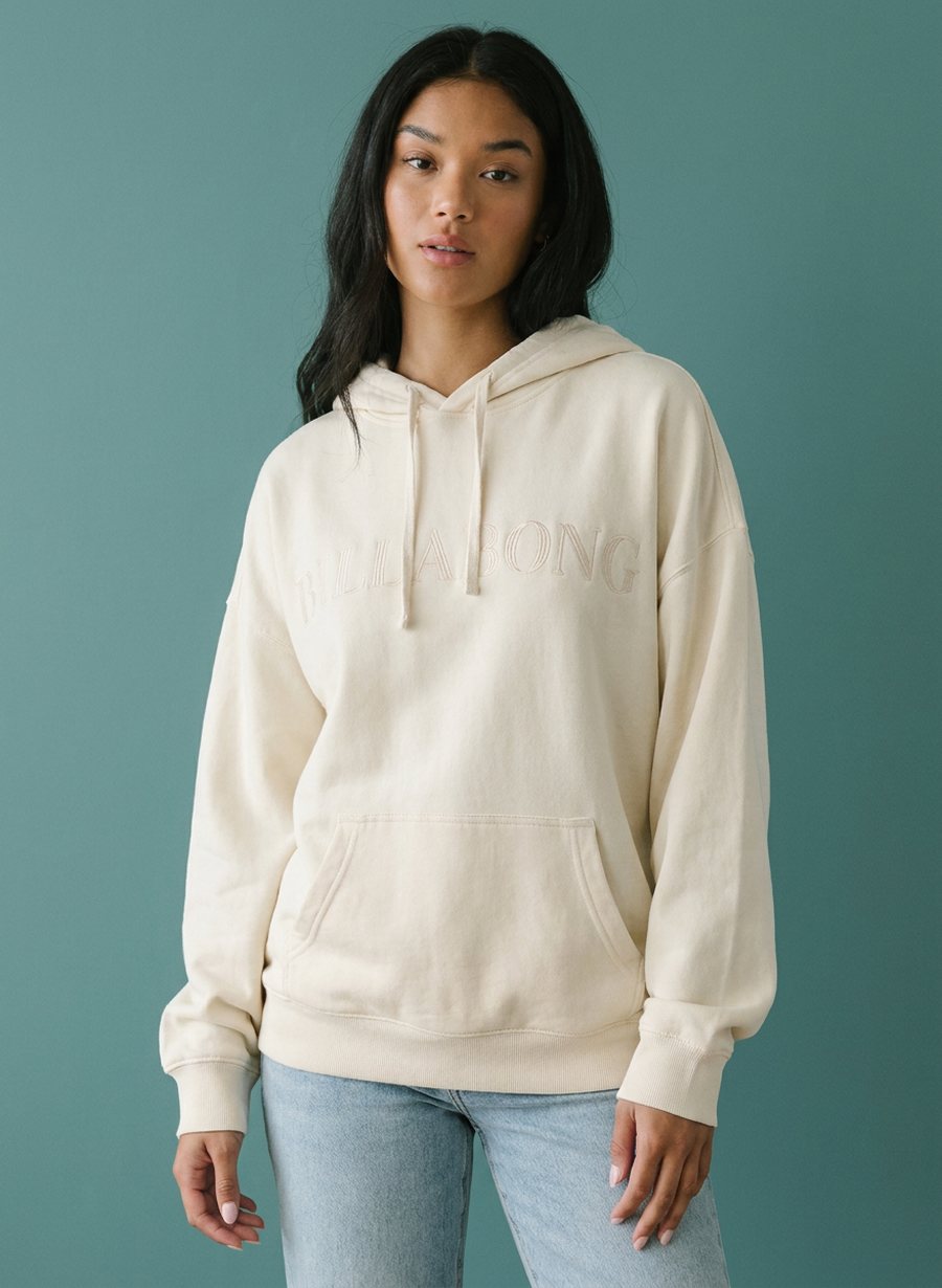 Woman in a cream Billabong pullover hoodie against a slate blue backdrop